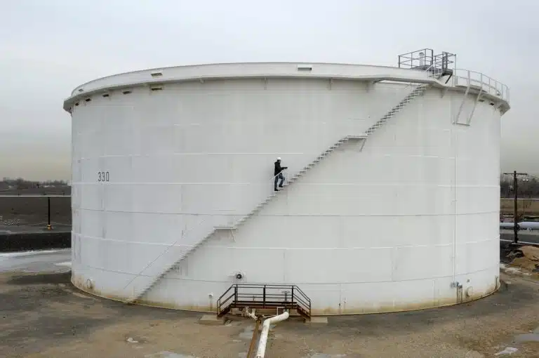 a large oil and gas storage tank with an employee walking up the staircase on the side