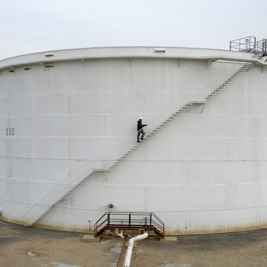 a large oil and gas storage tank with an employee walking up the staircase on the side